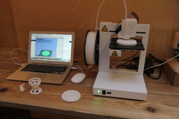 A 3D printer on a workbench next to a laptop