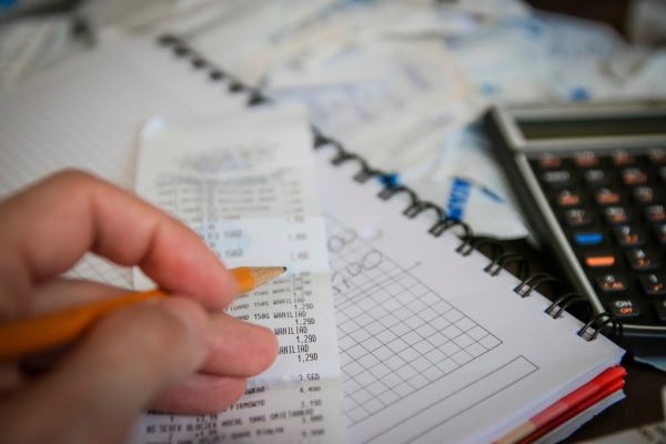 Hand mit Bleistift prüft Belege neben einem Taschenrechner